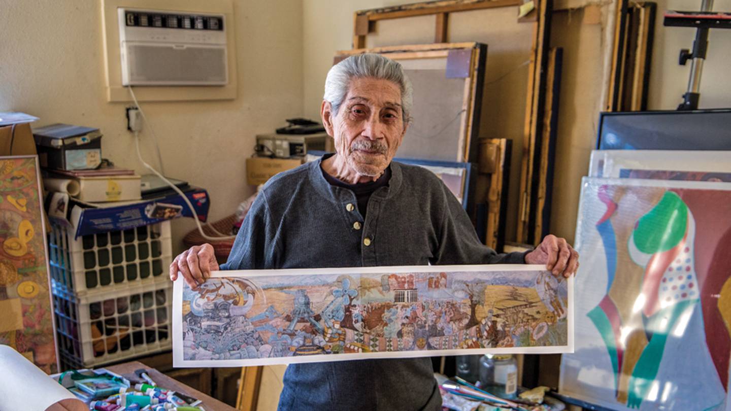 The artist Gilberto Guzman stands holding a small printout version of his mural "Multicultural."